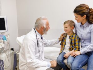 Paediatric doctor speaking with a young boy and his mother during a clinic consultation.